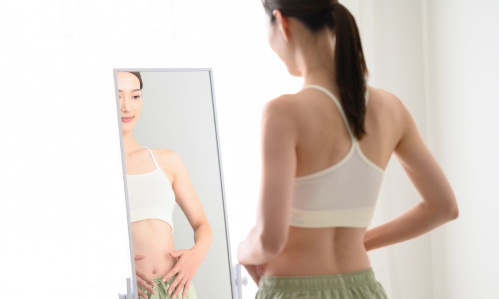 鏡を見てお腹のビフォーアフターを確認する女性